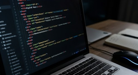 Laptop screen filled with lines of HTML and JavaScript code in a dark editor, representing web development